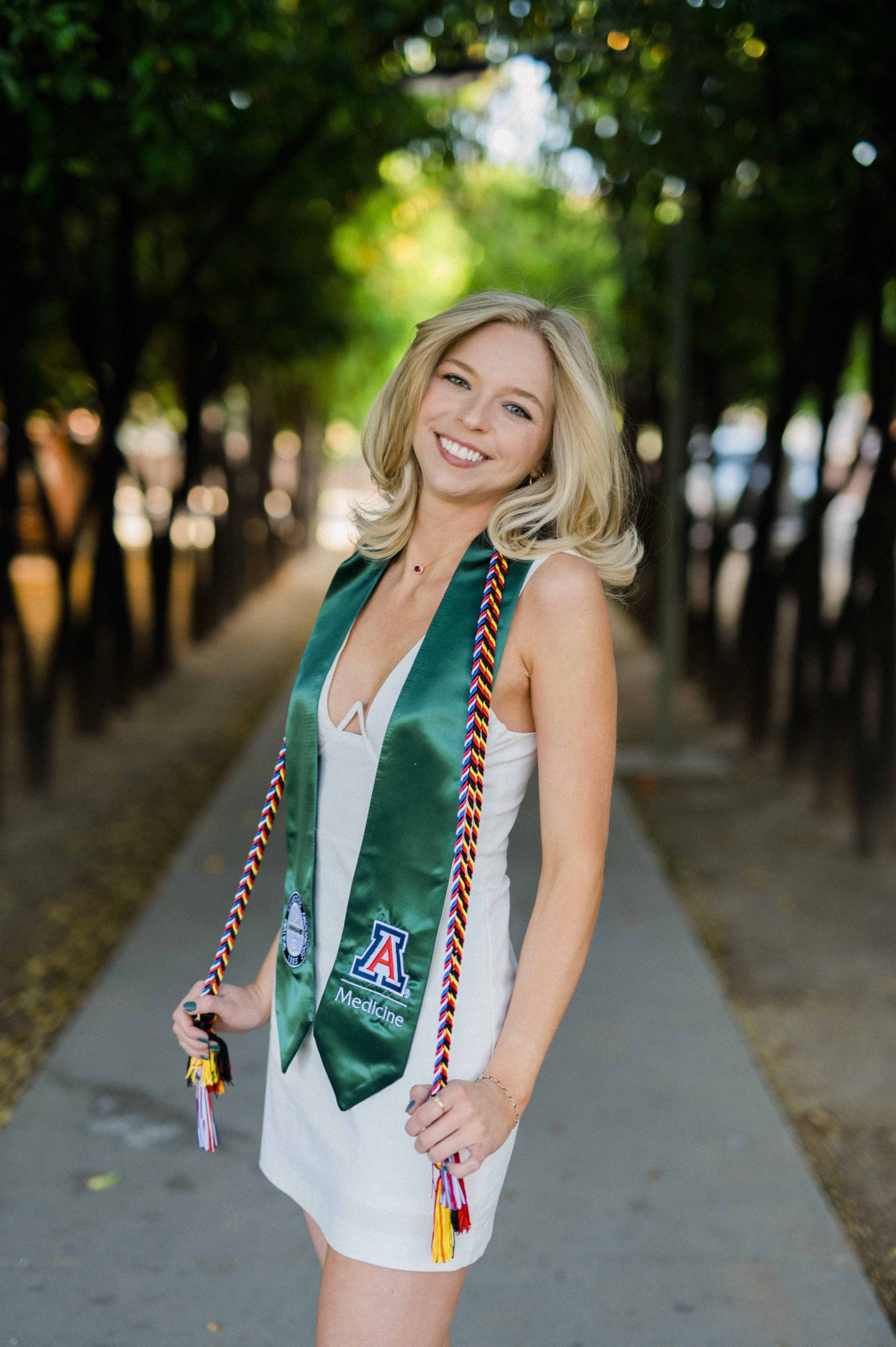 University of Arizona Graduation Picture with white dress cord and university sash standing in front of trees