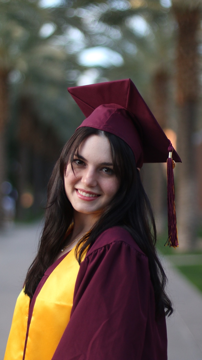 Close up portrait of smiling graduate in maroon cap and gown on a palm tree lined campus path