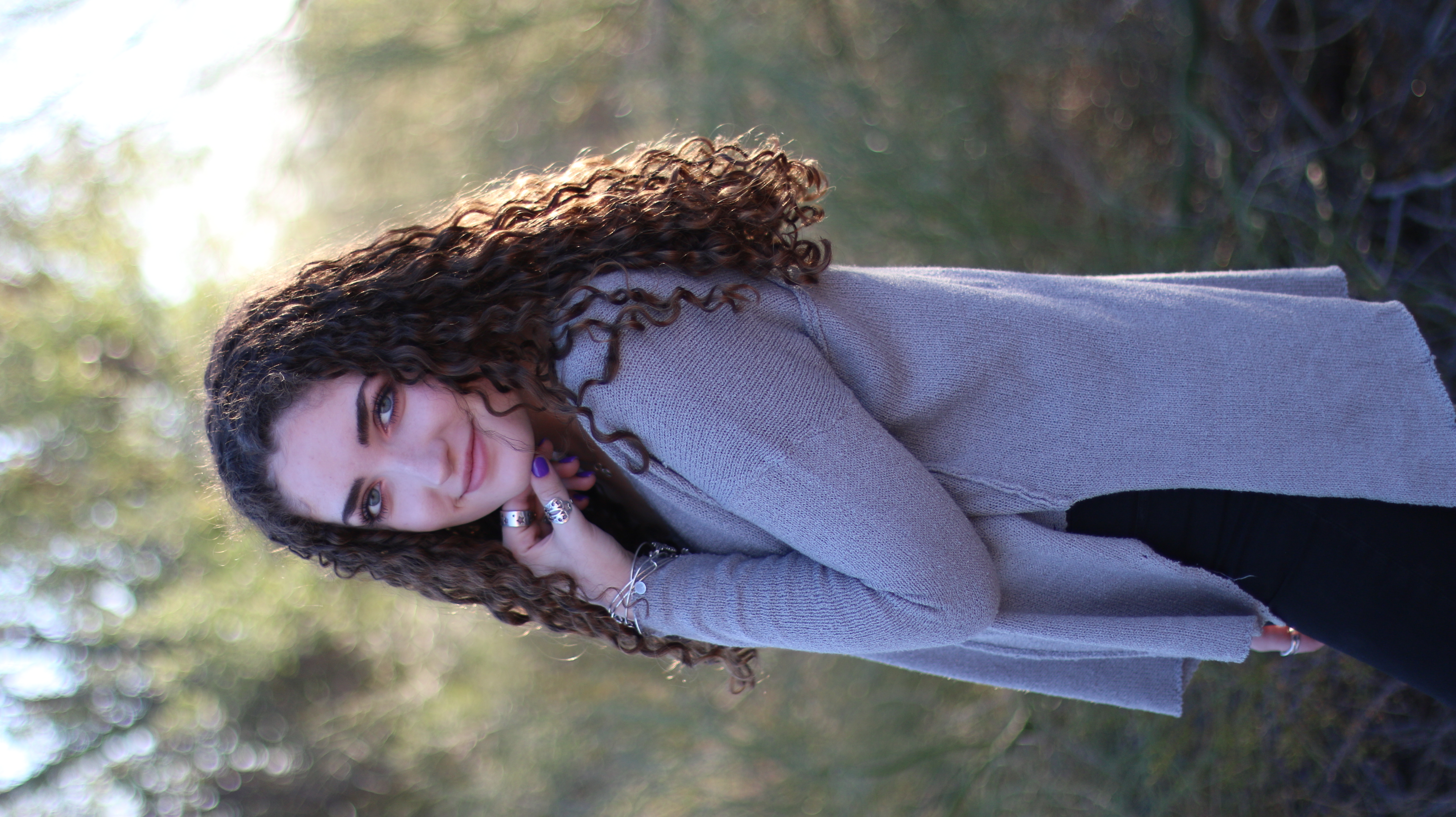 Young woman with curly brown hair smiling over her shoulder in a golden hour field