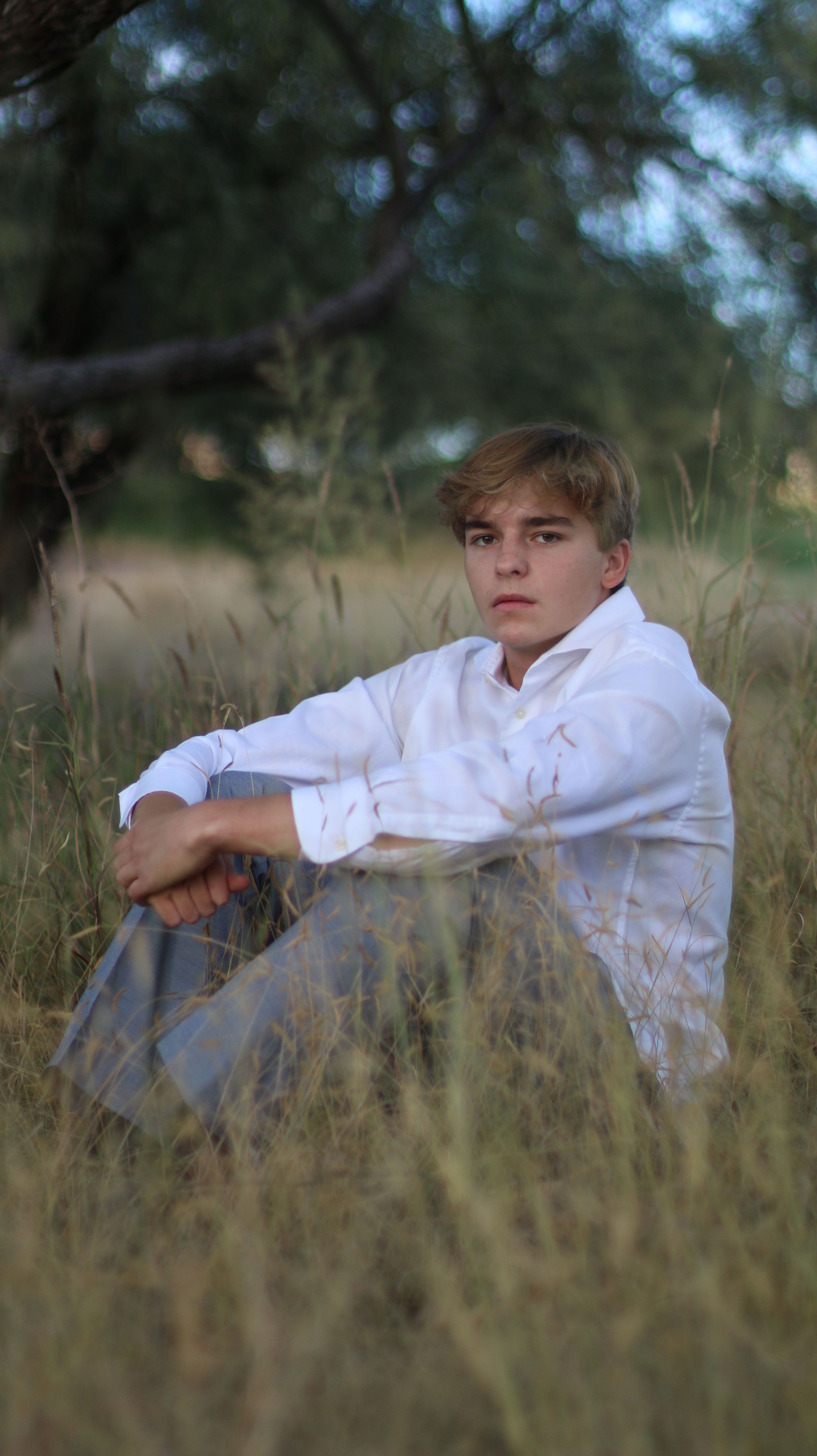 Young man in white button down shirt sitting in tall grass looking at the camera