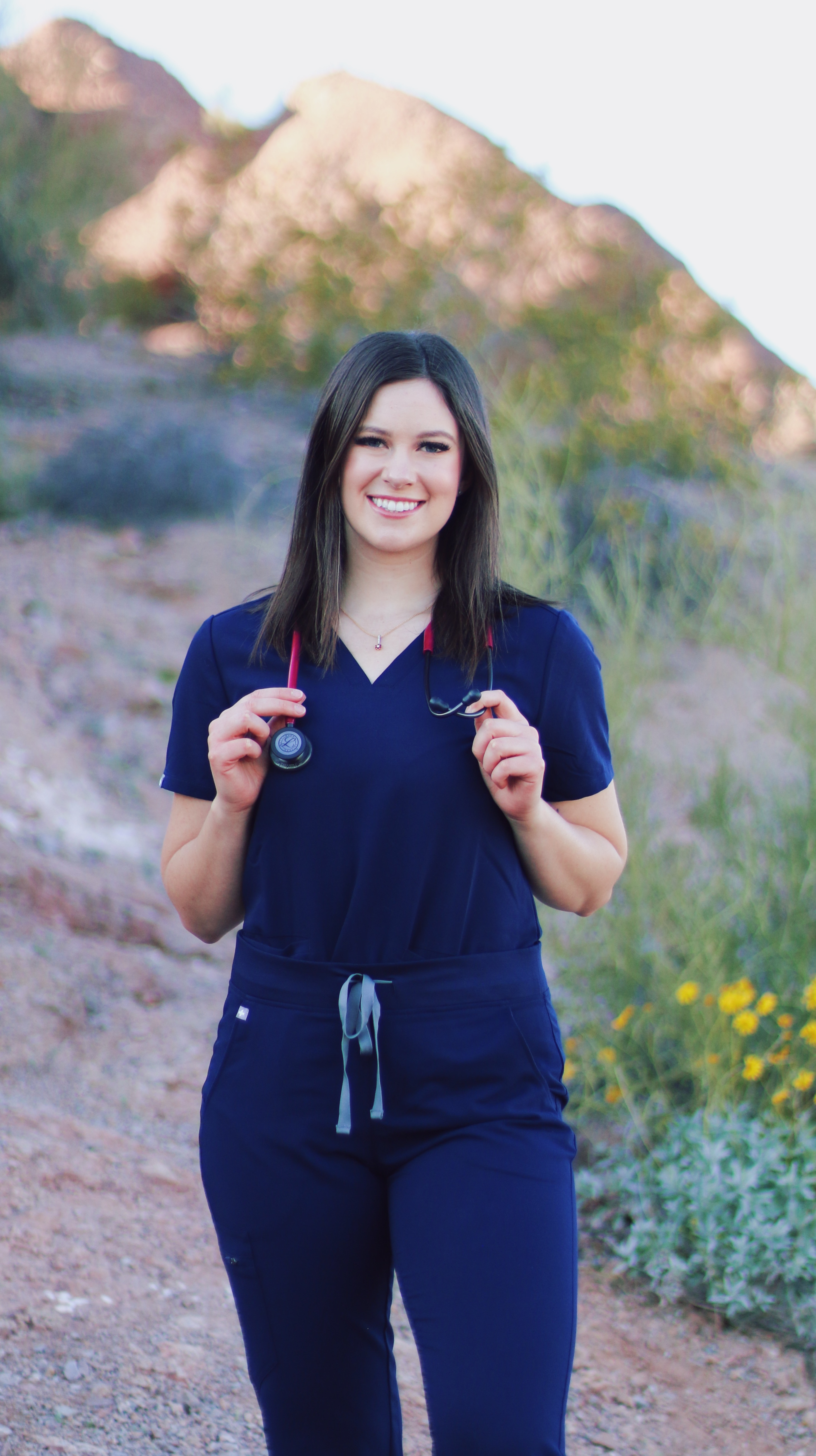 Woman in navy scrubs holding a stethoscope while standing on a desert trail at Papago Park