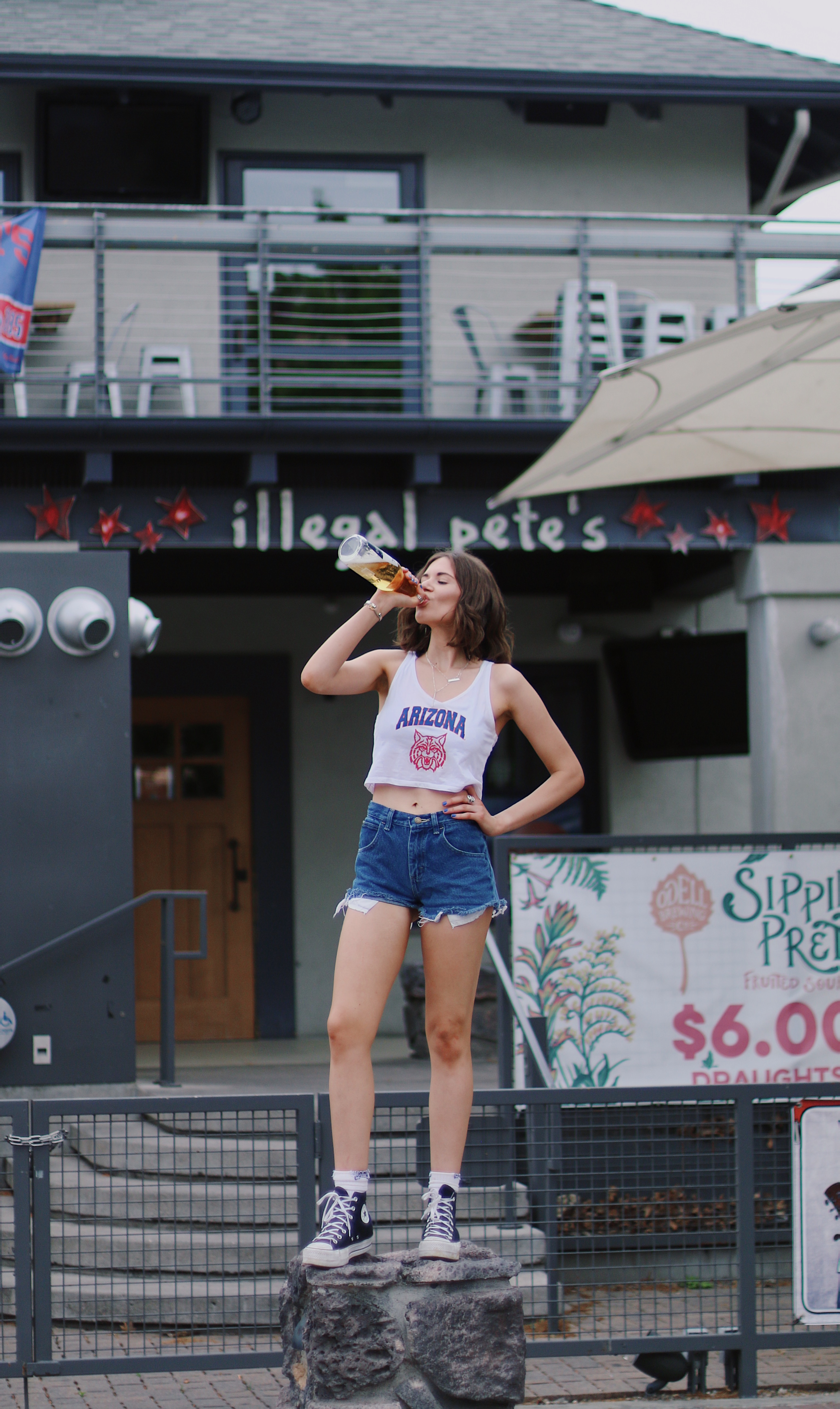 Young woman in Arizona Wildcats tank top standing on rocks outside Illegal Pete's restaurant