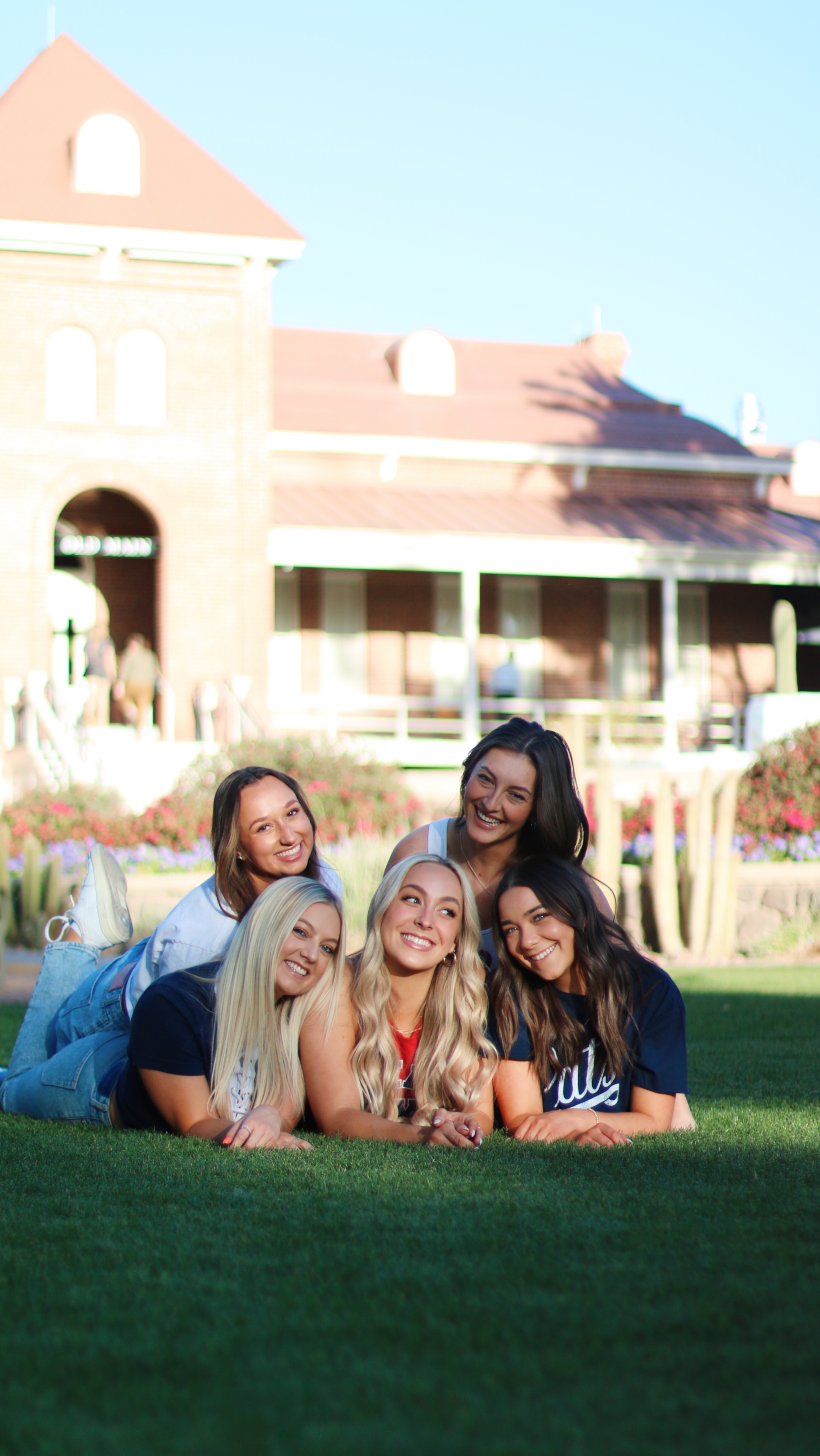 Group of graduates lawning down together in grass in front of a brick building