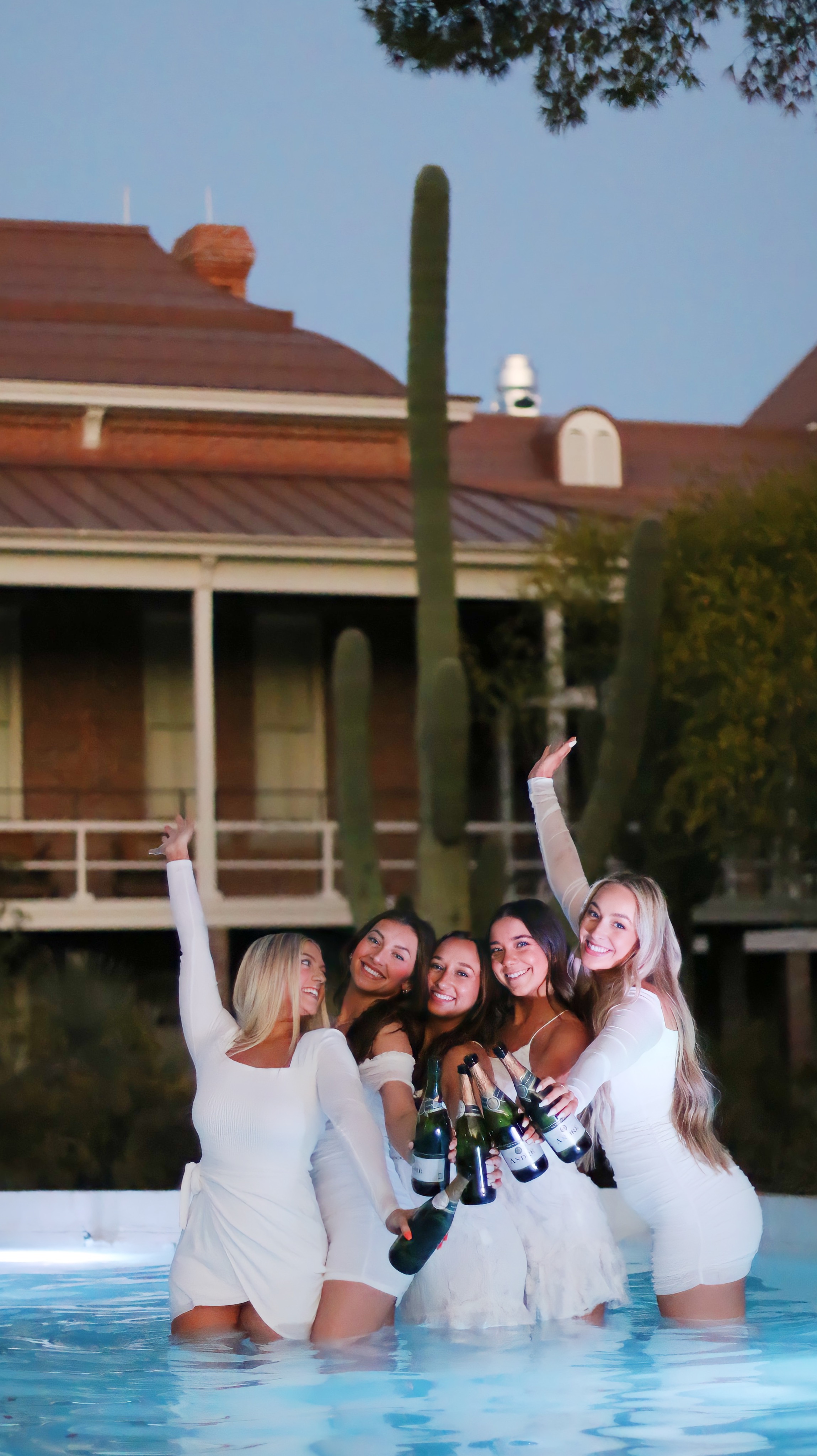 Graduates in white dresses toasting with champagne bottles in the fountain