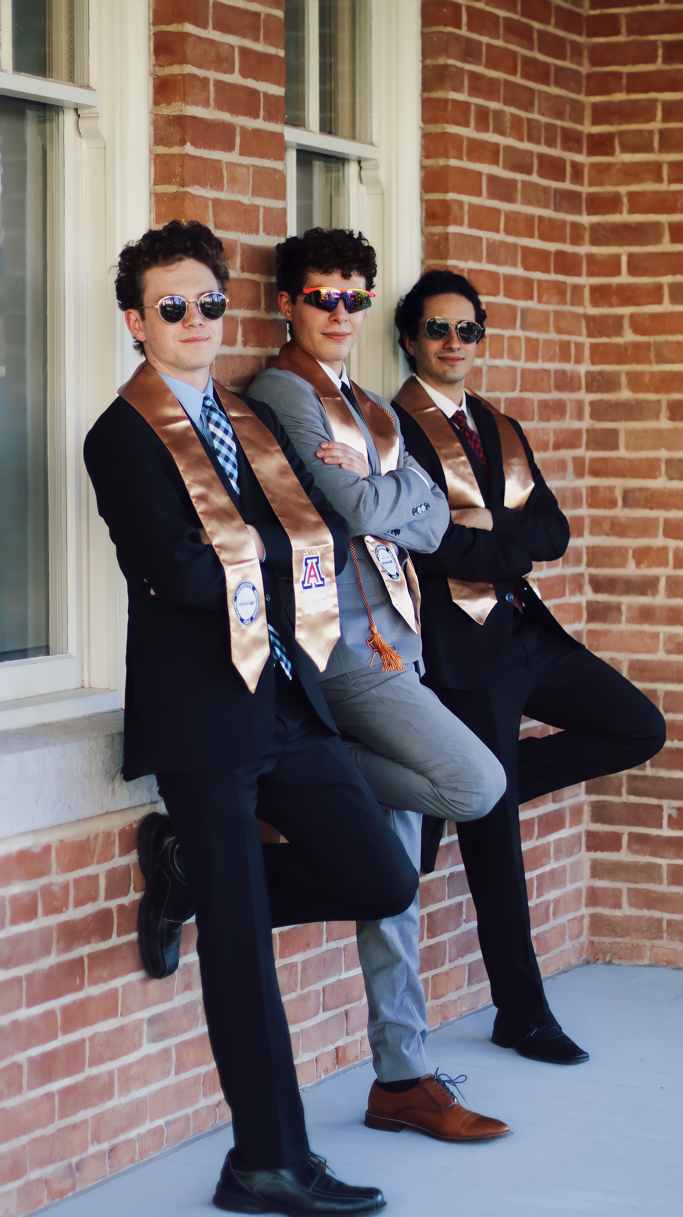 Group of graduate men leaning on the railing of a covered walkway with their arms crossed and looking at the camera