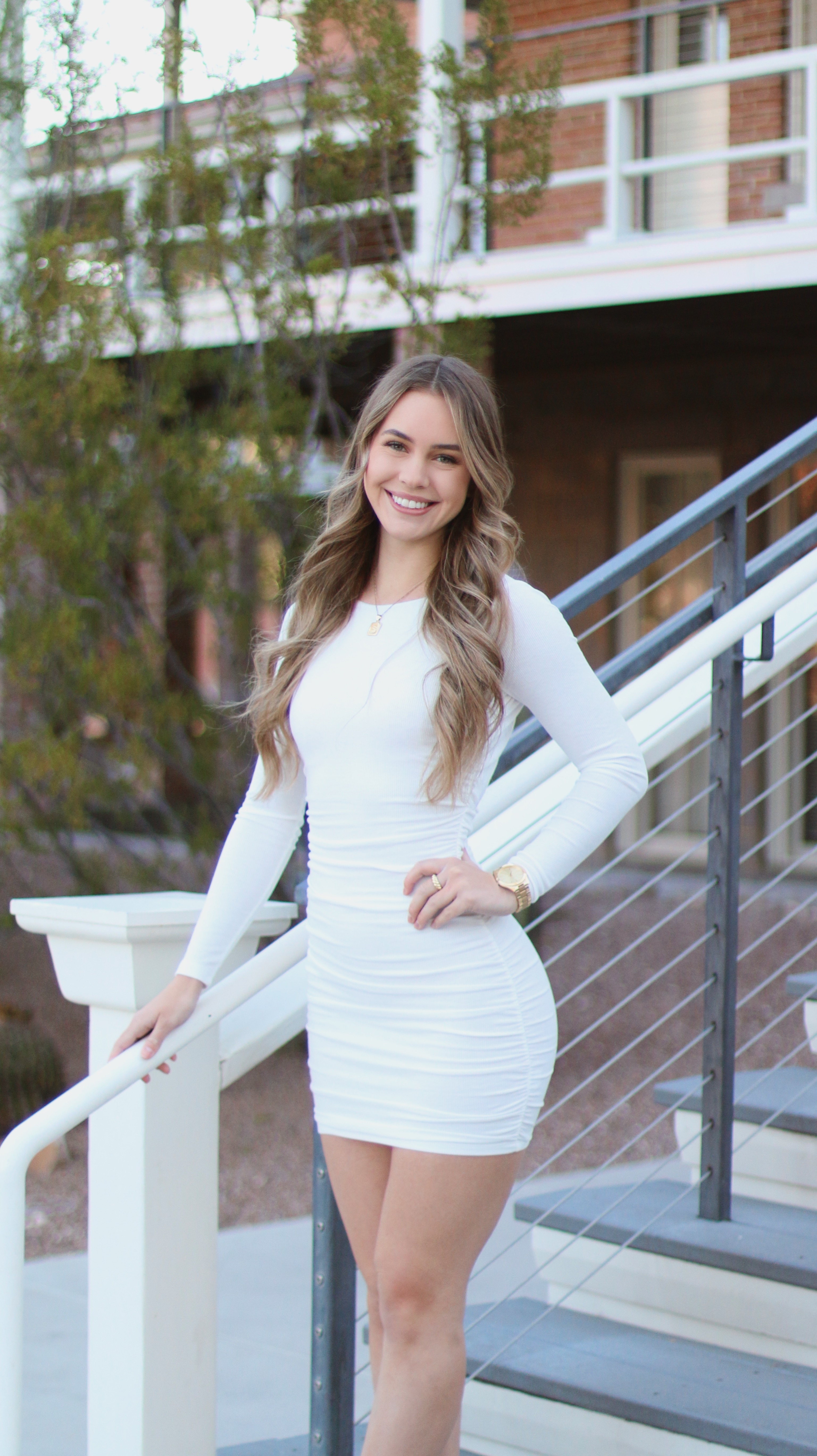 Graduate women posing in a white dress on the steps of a brick building