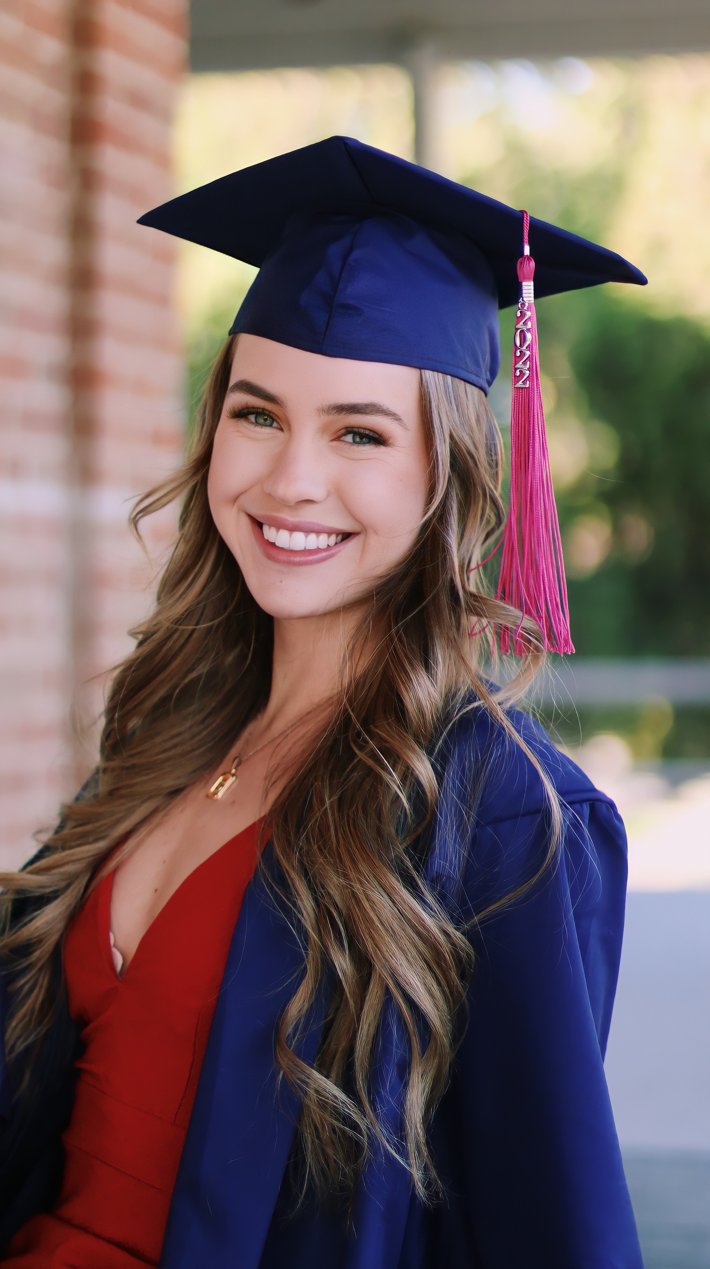 Close up of a women graduating with her cap and gown on smiling at the camera with a brick wall in the background