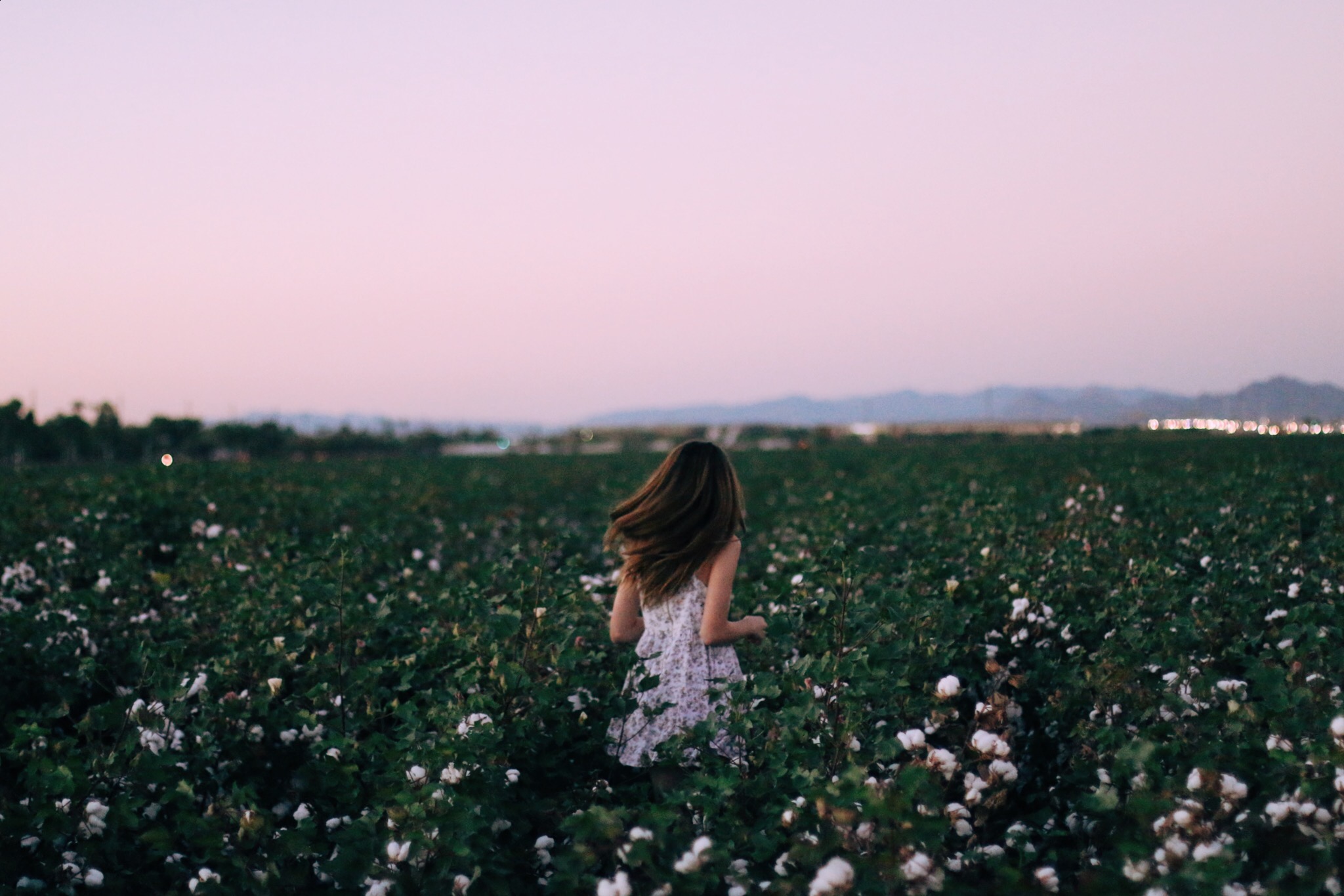 Women in a white dress running in a field away from the camera