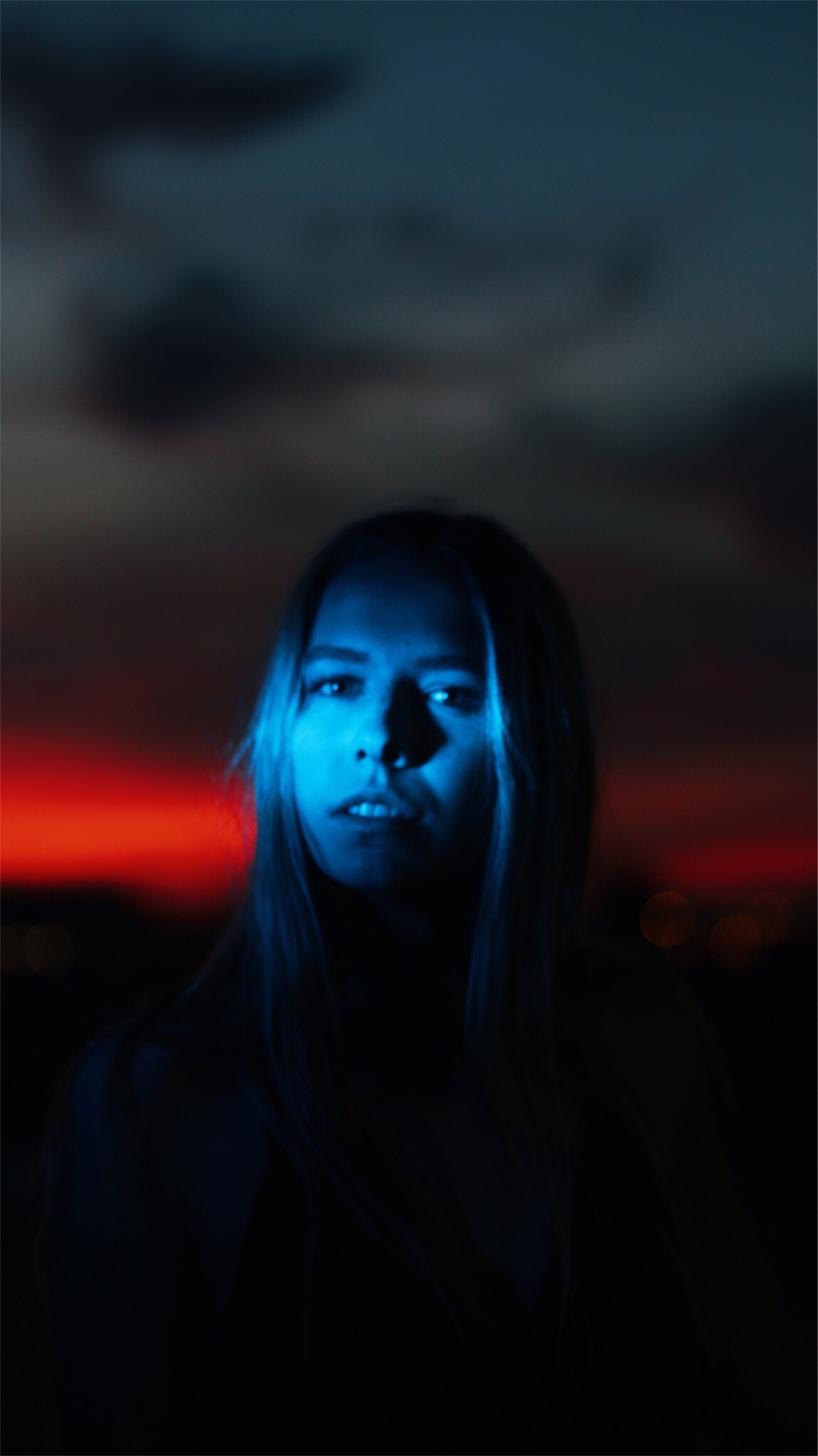 Young women posing in a red dress on the top of a building at sunset with dramatic lighting