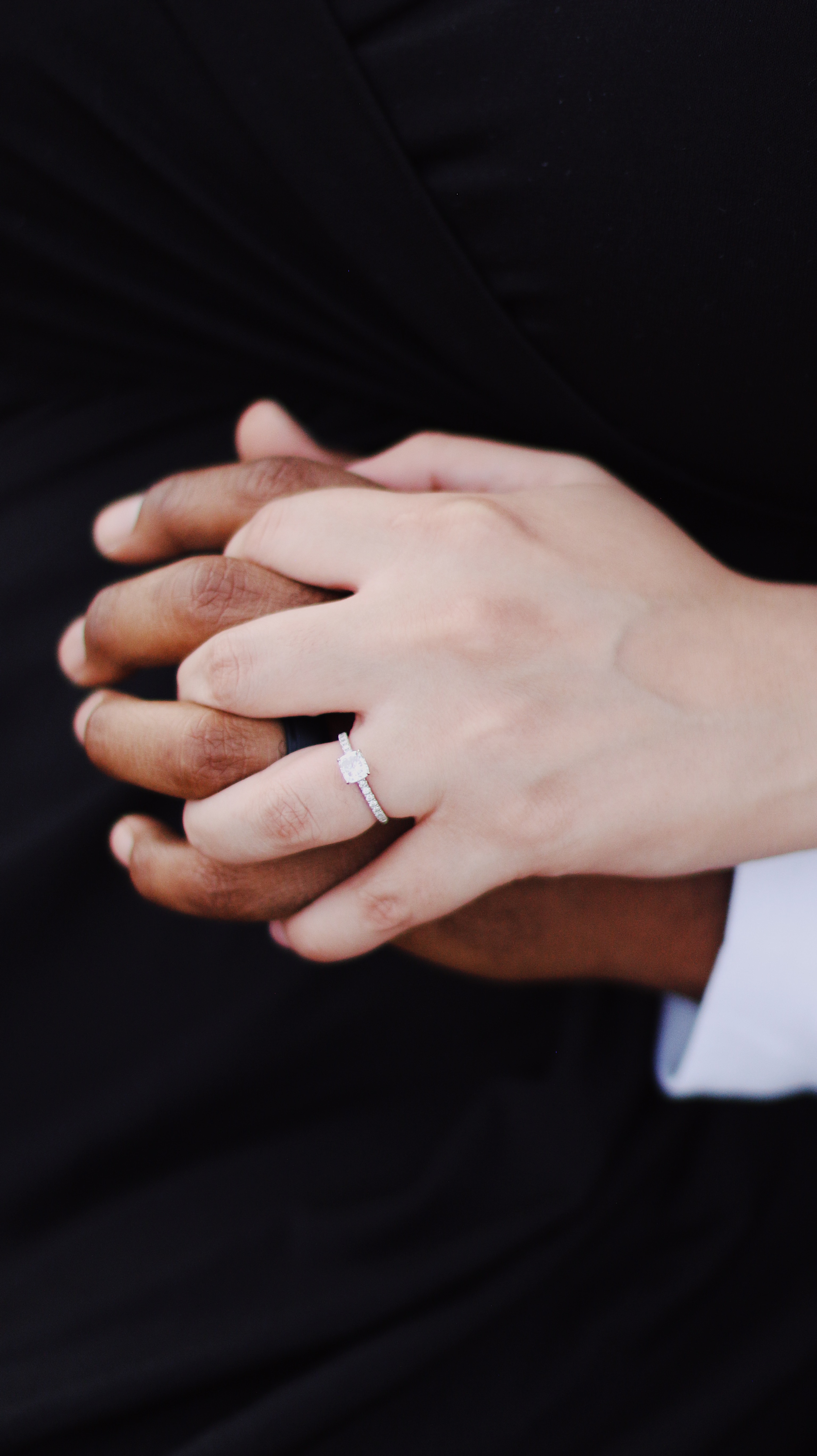 Close up of engagement rings on hands holding with a black background