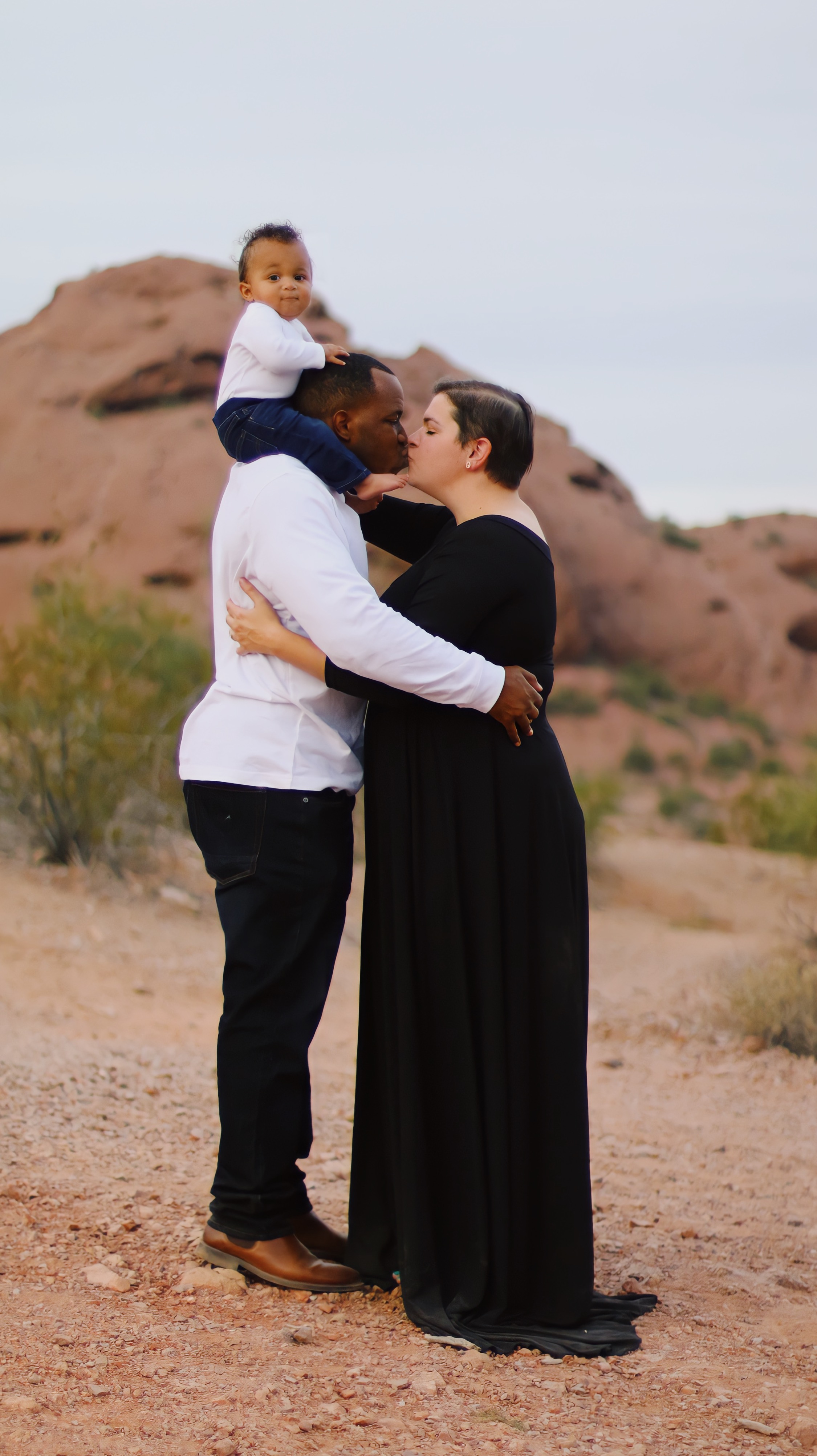 Family of three with the baby on the dad's shoulders and the mom and dad embracing