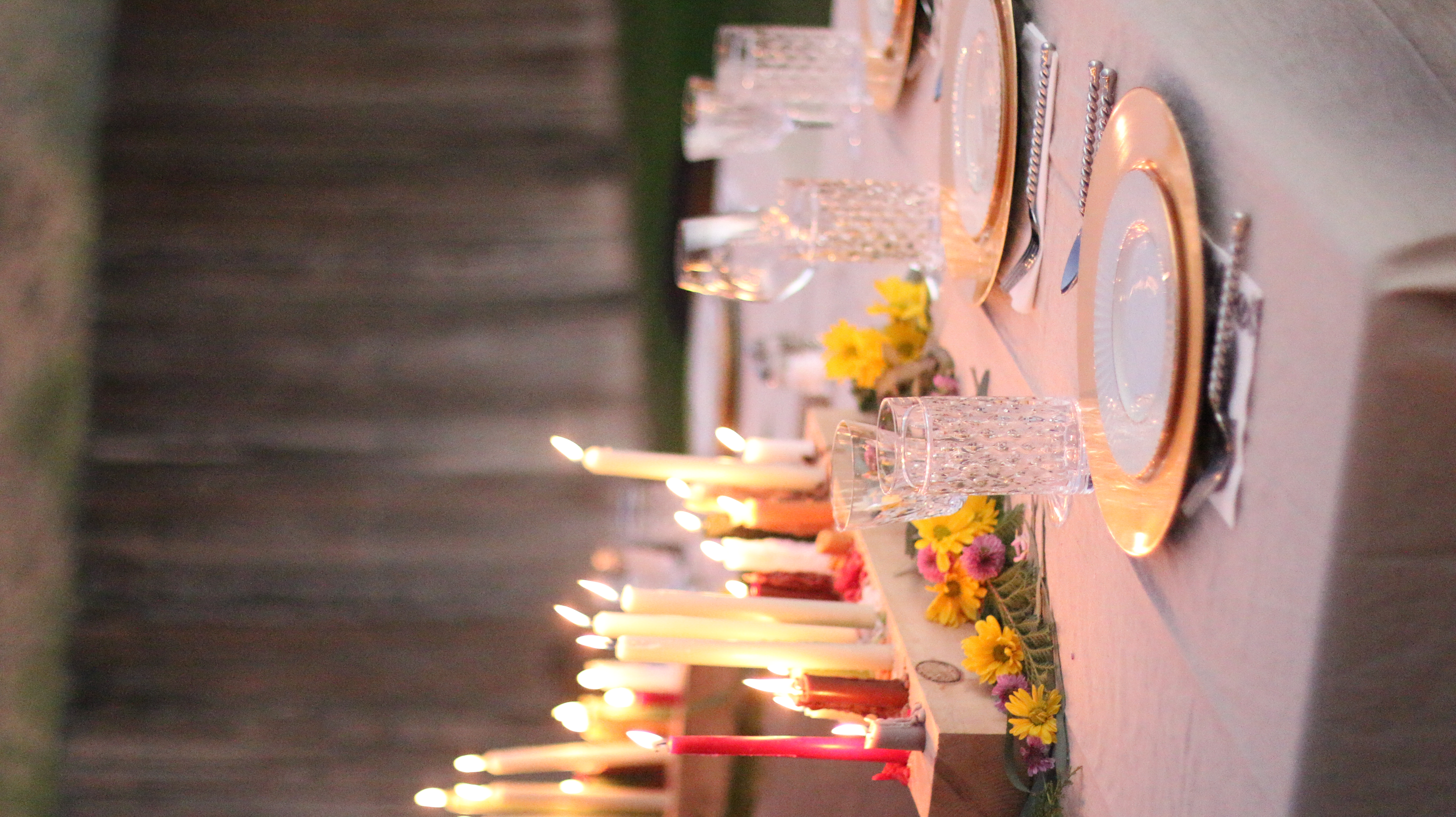 table setting on a beige tablecloth with a vase of flowers and a candle in the middle of the table